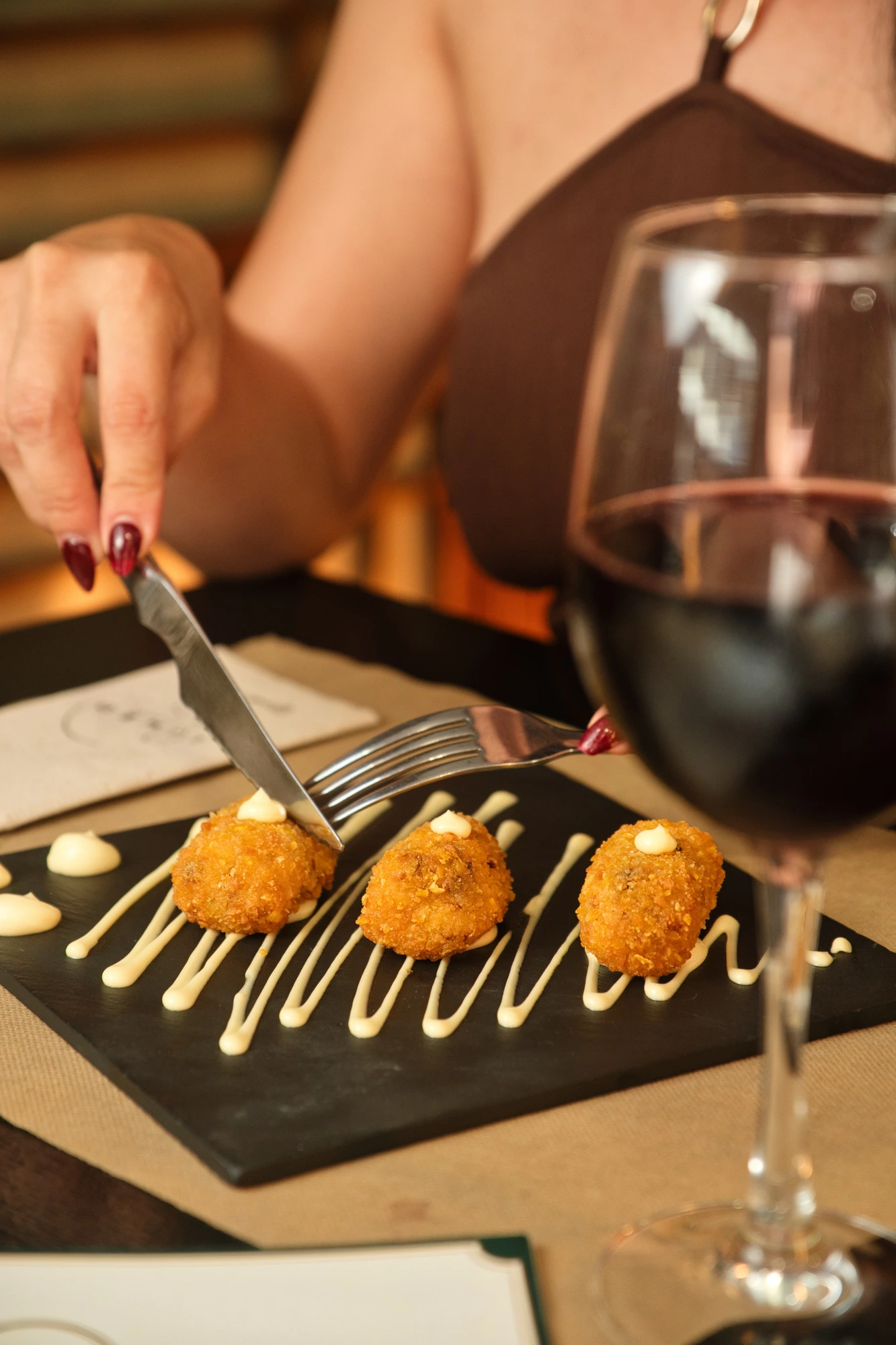 Croquetas caseras con una copa de vino tinto mientras una persona comparte mesa en Limbo